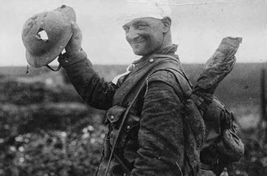 Lucky British soldier shows off his damaged helmet, 1917