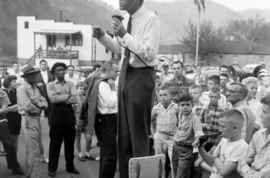 John F. Kennedy campaigns in rural West Virginia, precariously perched on a high-chair to deliver his speech, 1960