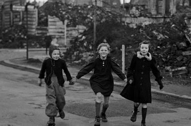 Three schoolgirls skating home from school while passing blocks of destroyed houses in Essen, 194